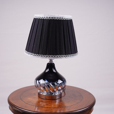 An elegant table lamp with a chic twisted silver base and a classic black lampshade. Equipped with an E27 LED light, it casts a warm and sophisticated glow.