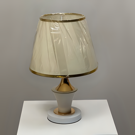 Modern white and gold table lamp with a flared lampshade and a sculpted curved base, placed on a white table.

