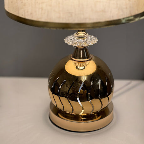 table lamp with a round metallic gold base, placed on a white table.