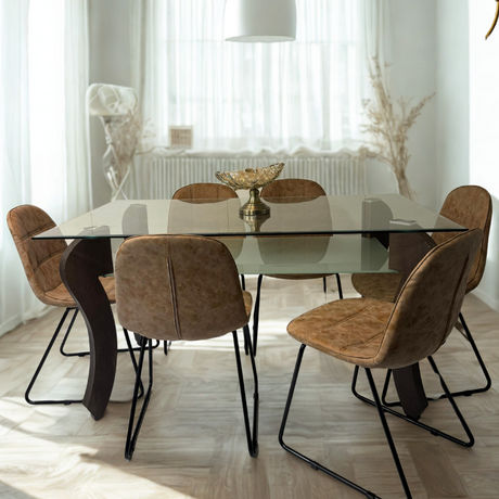 A sunlit dining room featuring a glass dining table with curved brown legs and six brown chairs on a light herringbone floor.
