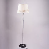 Classic floor lamp with a white embroidered shade and a slim black and silver stand, positioned against a neutral background.