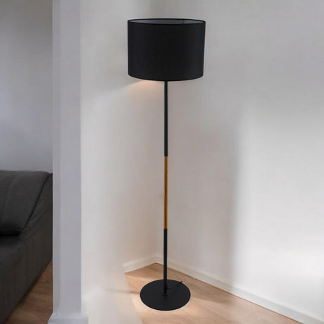 A tall, slim black floor lamp with a black cylindrical lampshade and wooden accents, standing in a modern living space.