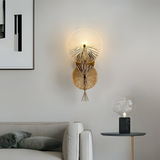 Modern decorative wall light with two fan-like glass discs on a gold mount, installed above a neutral-toned sofa and beside a sleek black side table with a translucent glass lamp.