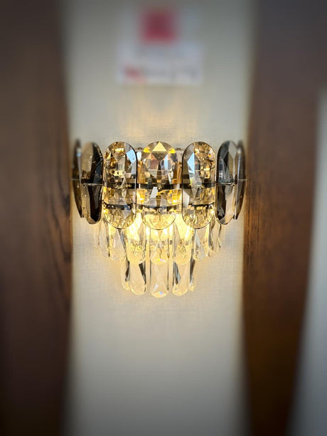A decorative gold wall light featuring grey circular elements with cascading crystal droplets, reflecting warm light beautifully.
