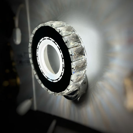  round wall sconce with a outer ring and embedded crystals, glowing from the center.