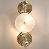 A stylish dual-wall sconce with circular, pleated white glass diffusers and gold accents, mounted on a beige wall.
