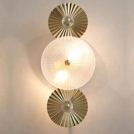 A stylish dual-wall sconce with circular, pleated white glass diffusers and gold accents, mounted on a beige wall.

