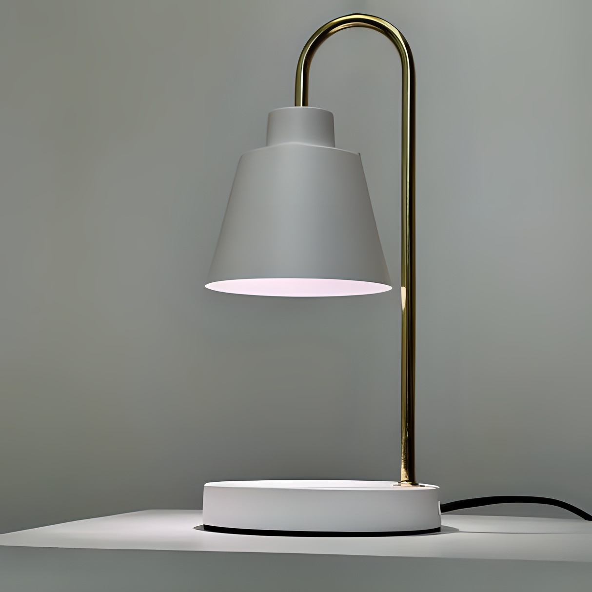 The desk lamp features a sleek and minimalist design with a white lampshade resting on a slender gold stand. The stand curves from a circular white base.  Positioned against a neutral background.