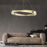 A modern gold and crystal circular chandelier hanging in a living room with a beige couch in the background.