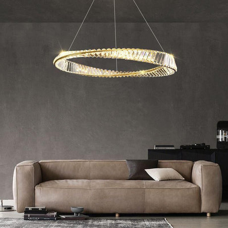 A modern gold and crystal circular chandelier hanging in a living room with a beige couch in the background.