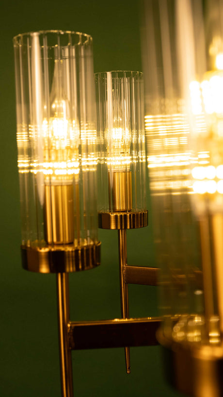 close up of a metal chandelier with symmetrical geometric arms and vertical glass shades against a green wall 