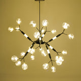 Modern starburst-style chandelier with multiple crystal-glass bulb covers on black and gold arms, emitting warm white light. 