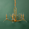 A vintage-inspired gold chandelier with delicate curved arms and candle-style bulbs, hanging against a green background.
