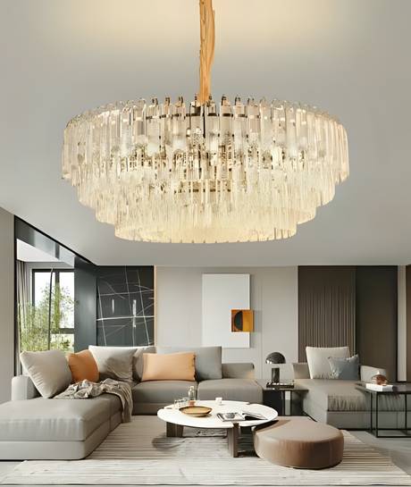 Luxurious round crystal chandelier with cascading glass elements suspended from a central fixture, illuminating a contemporary living room with neutral-toned sectional sofas, modern art, and minimalist decor.