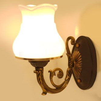 A brass wall sconce with a curved arm and a white fluted glass shade, blending modern and traditional elements.