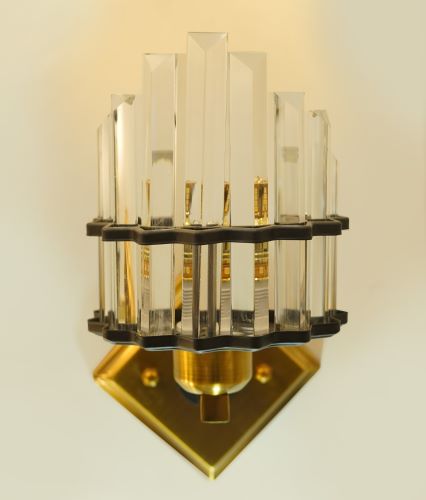 A wall-mounted light with a gold-toned base and crystal rods forming a structured yet elegant design. The angled mounting plate adds a unique dimension to the fixture.