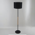 A contemporary black floor lamp with a cylindrical black lampshade and wooden details, set against a plain white background.