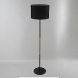 A contemporary black floor lamp with a cylindrical black lampshade and wooden details, set against a plain white background.