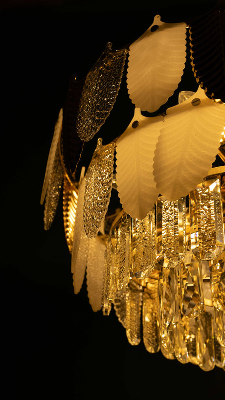 A detailed shot of the chandelier's intricate design, showcasing layered gold, white, and clear glass leaves reflecting light beautifully.