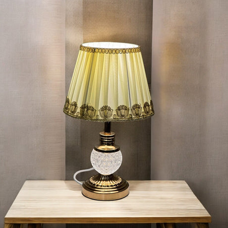 Classic gold and crystal table lamp with a delicate patterned fabric shade, equipped with an E27 LED bulb. The base features a gold finish with a built-in LED light inside the glass, enhancing its elegant design.