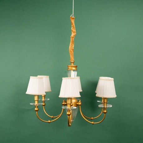 A golden chandelier with multiple curved arms, each holding a white pleated lampshade with decorative trim. the chandelier features a central glass column and is suspended from a gold-colored rod.