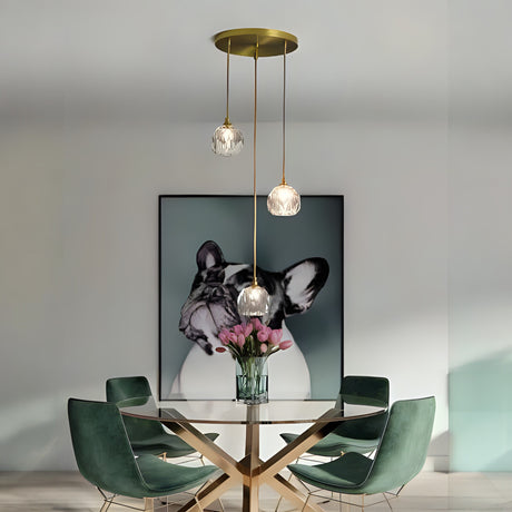 A minimalistic pendant light setup featuring three transparent glass globes with gold accents, hanging above a dining table with a framed dog artwork in the background.