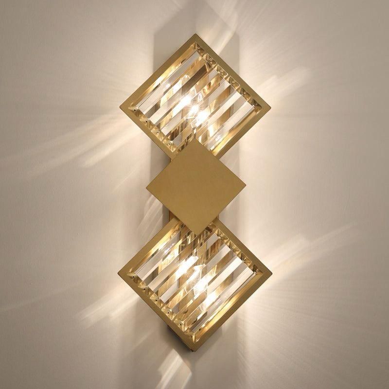 A gold and crystal geometric wall sconce with two square-shaped crystal elements emitting warm light.
