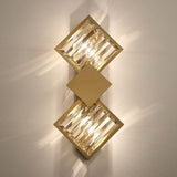 A gold and crystal geometric wall sconce with two square-shaped crystal elements emitting warm light.
