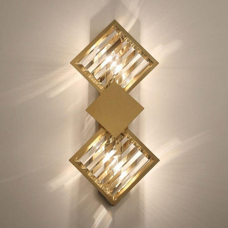 A gold and crystal geometric wall sconce with two square-shaped crystal elements emitting warm light.
