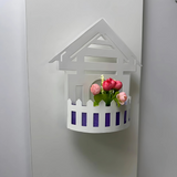 Wall-mounted LED light fixture designed in the shape of a white house , featuring a cork-style built-in compartment holding artificial pink and red tulip flowers.