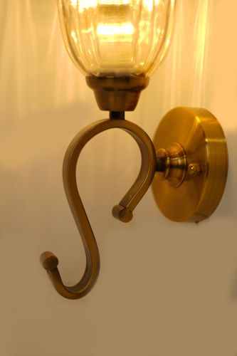A metal wall sconce with an elegantly curved arm and a round wall mount, supporting a glass shade.
