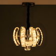 A modern crystal pendant chandelier featuring geometric curved glass segments illuminated with warm white light, suspended from a twisted black cord and chrome ceiling mount.