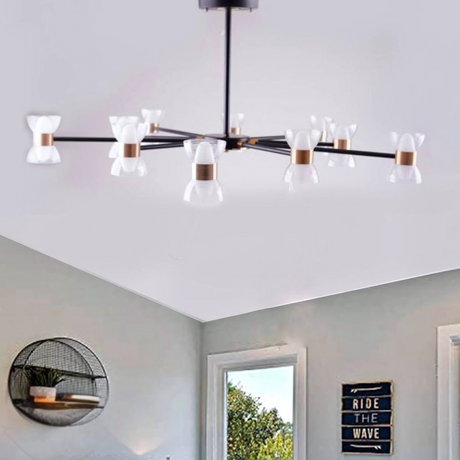 A sleek black linear chandelier with multiple arms, each adorned with a small white conical glass shade, mounted on a square ceiling base. The fixture is installed on a white ceiling in a stylish bedroom room featuring minimalist decor , and a decorative sign that reads 'Ride The Wave'.