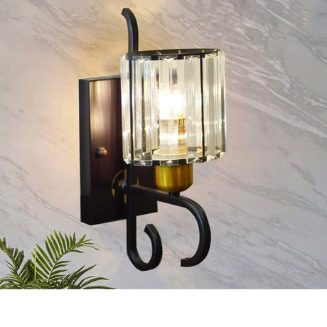 This stylish fixture features a brown metal base, a curved arm, and a cylindrical glass shade with gold accents on a marble wall. The lighting effect is soft and diffused.
