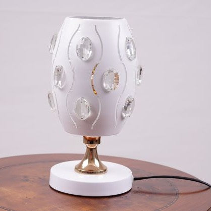 A white globe table lamp with a geometric design, adorned with crystal beads, gold accents, and a sleek base, sits on a wooden table. It features an LED light with an E27 bulb, casting a warm, stylish glow.