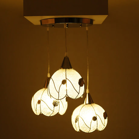 A trio of floral-inspired glass pendant lights, illuminated and emitting a warm golden glow.
