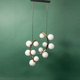 A gold chandelier with two curved metal arms, each adorned with frosted white glass globe lights, suspended from a black ceiling mount against a green background.
