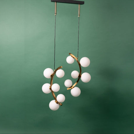 A gold chandelier with two curved metal arms, each adorned with frosted white glass globe lights, suspended from a black ceiling mount against a green background.
