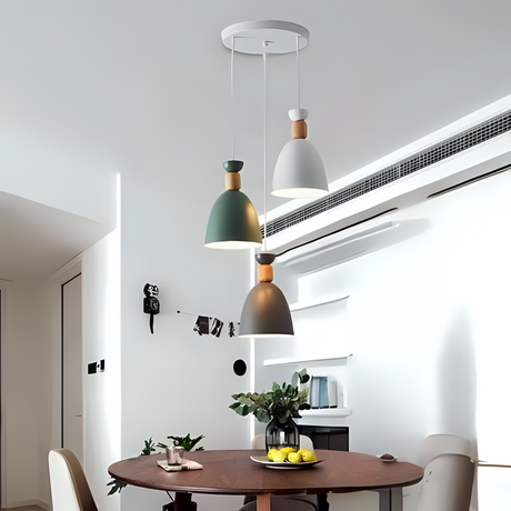A set of three pendant lights in green, white, and copper colors hanging from a white ceiling over a round dining table in a modern, minimalist dining room.