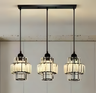 Three industrial-style pendant lights with black metal frames and glass shades, hanging from a black rectangular ceiling mount.

