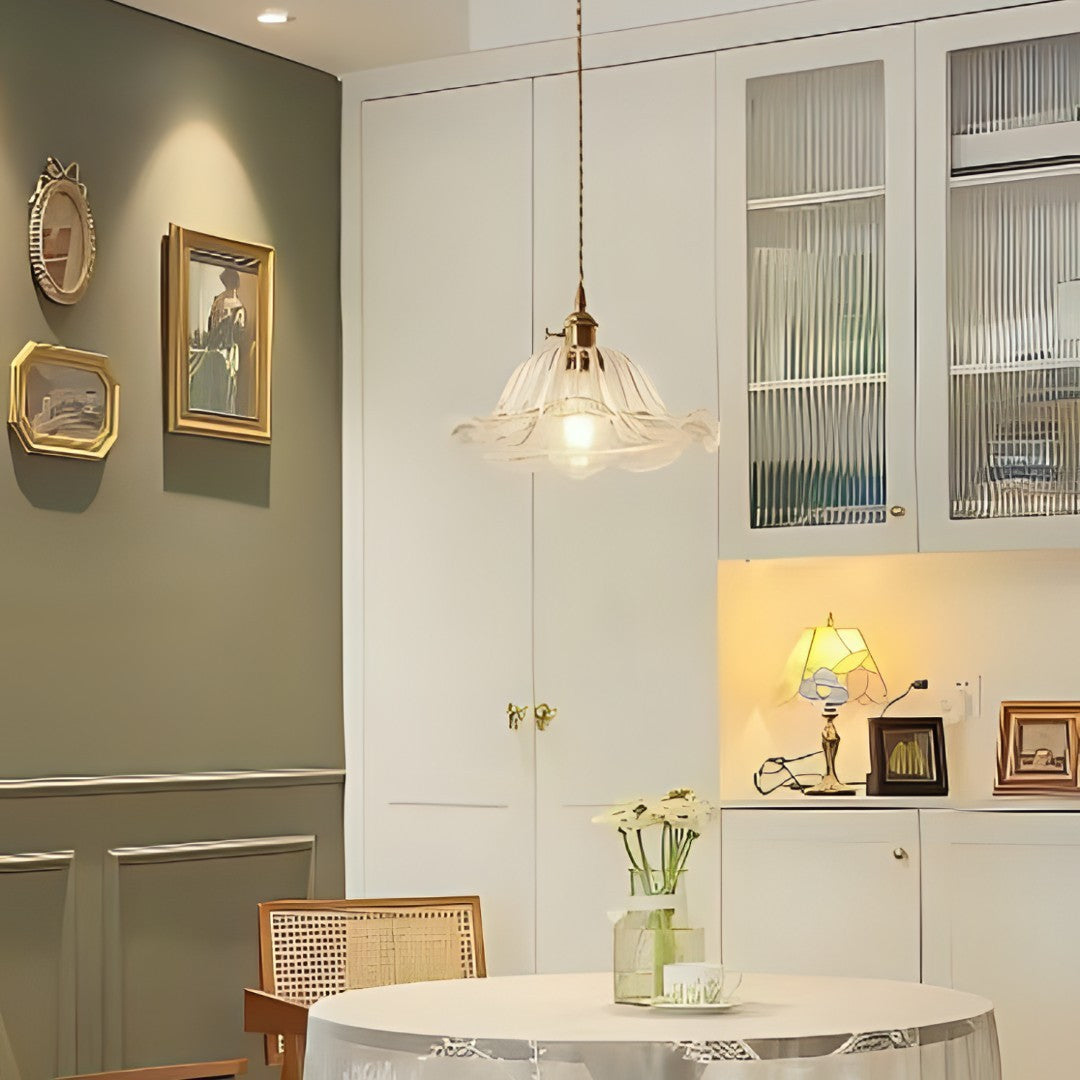 A vintage-style glass pendant light with gold accents hanging above a round dining table in a cozy kitchen space.
