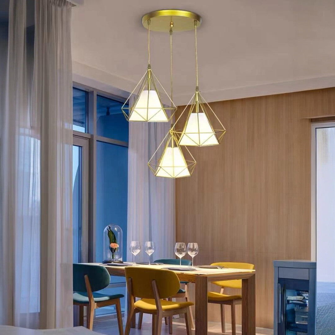 A cluster of golden triangular pendant lights suspended from a circular gold ceiling mount, positioned above a dining table with colorful chairs.