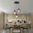 A set of hanging pendant lights with intricate cut-out patterns, suspended from a black ceiling mount over a modern kitchen dining area.