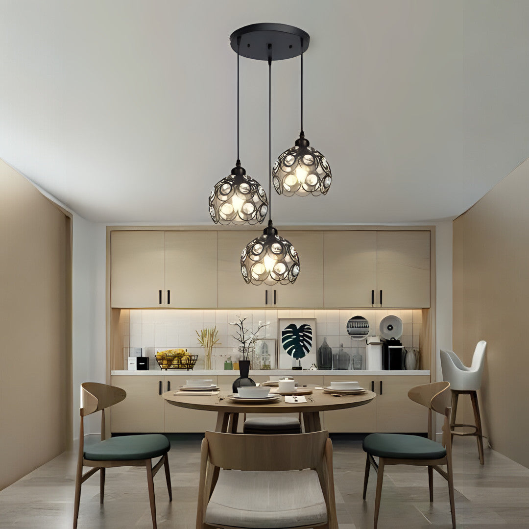 A set of hanging pendant lights with intricate cut-out patterns, suspended from a black ceiling mount over a modern kitchen dining area.
