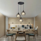 A set of hanging pendant lights with intricate cut-out patterns, suspended from a black ceiling mount over a modern kitchen dining area.