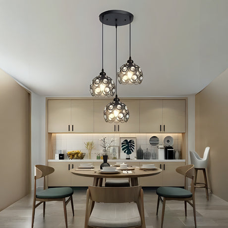 A set of hanging pendant lights with intricate cut-out patterns, suspended from a black ceiling mount over a modern kitchen dining area.