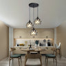 A set of hanging pendant lights with intricate cut-out patterns, suspended from a black ceiling mount over a modern kitchen dining area.