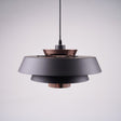 A modern layered pendant light with a matte black and copper finish, featuring a wide circular design with concentric discs, hanging from a black cord against a light gray background.