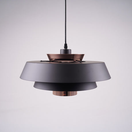 A modern layered pendant light with a matte black and copper finish, featuring a wide circular design with concentric discs, hanging from a black cord against a light gray background.