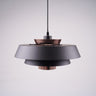 A modern layered pendant light with a matte black and copper finish, featuring a wide circular design with concentric discs, hanging from a black cord against a light gray background.